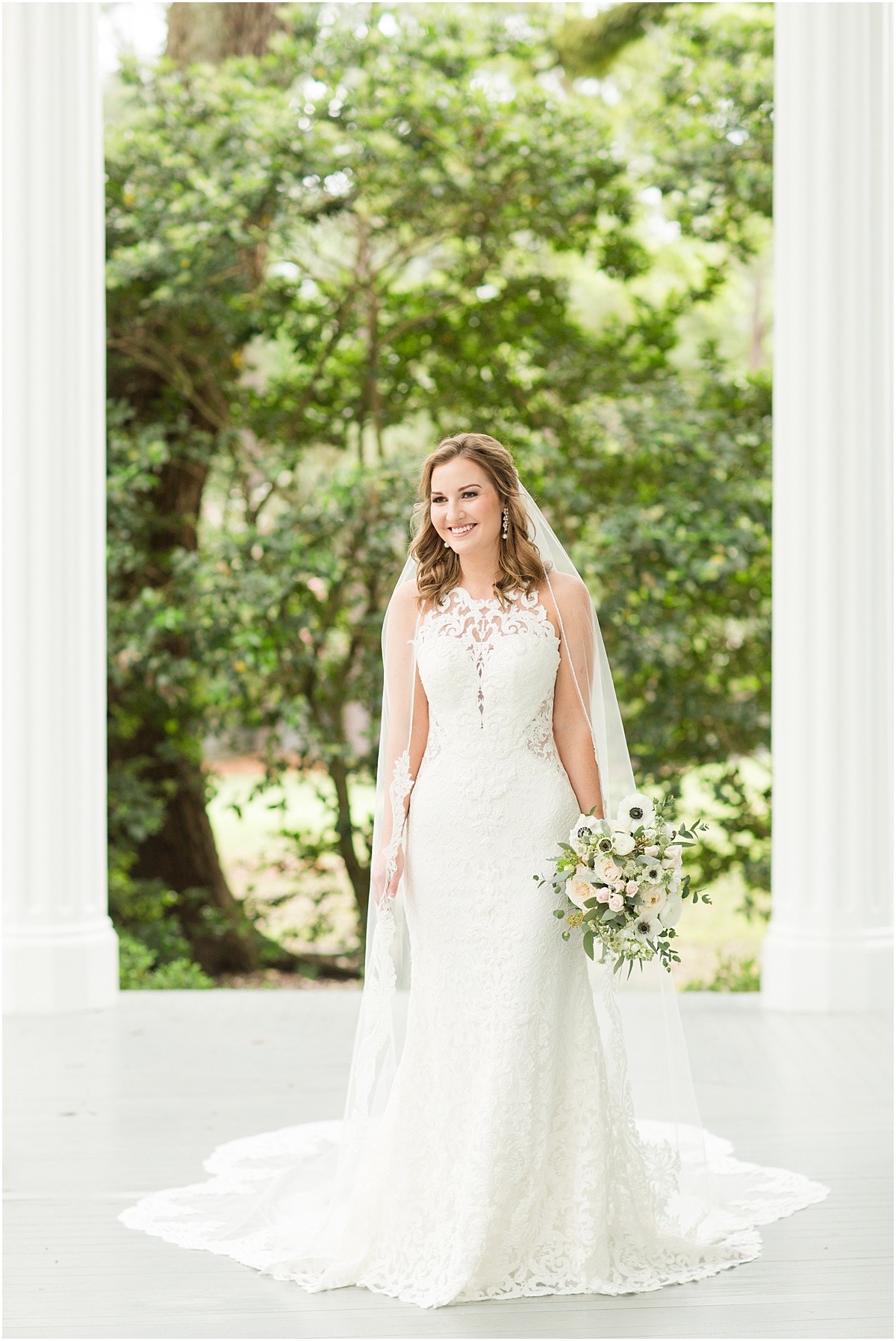 Bride wearing a lace gown and cathedral length veil, holding a pastel spring bouquet, standing on the porch at the Bragg-Mitchell Mansion in Mobile Alabama