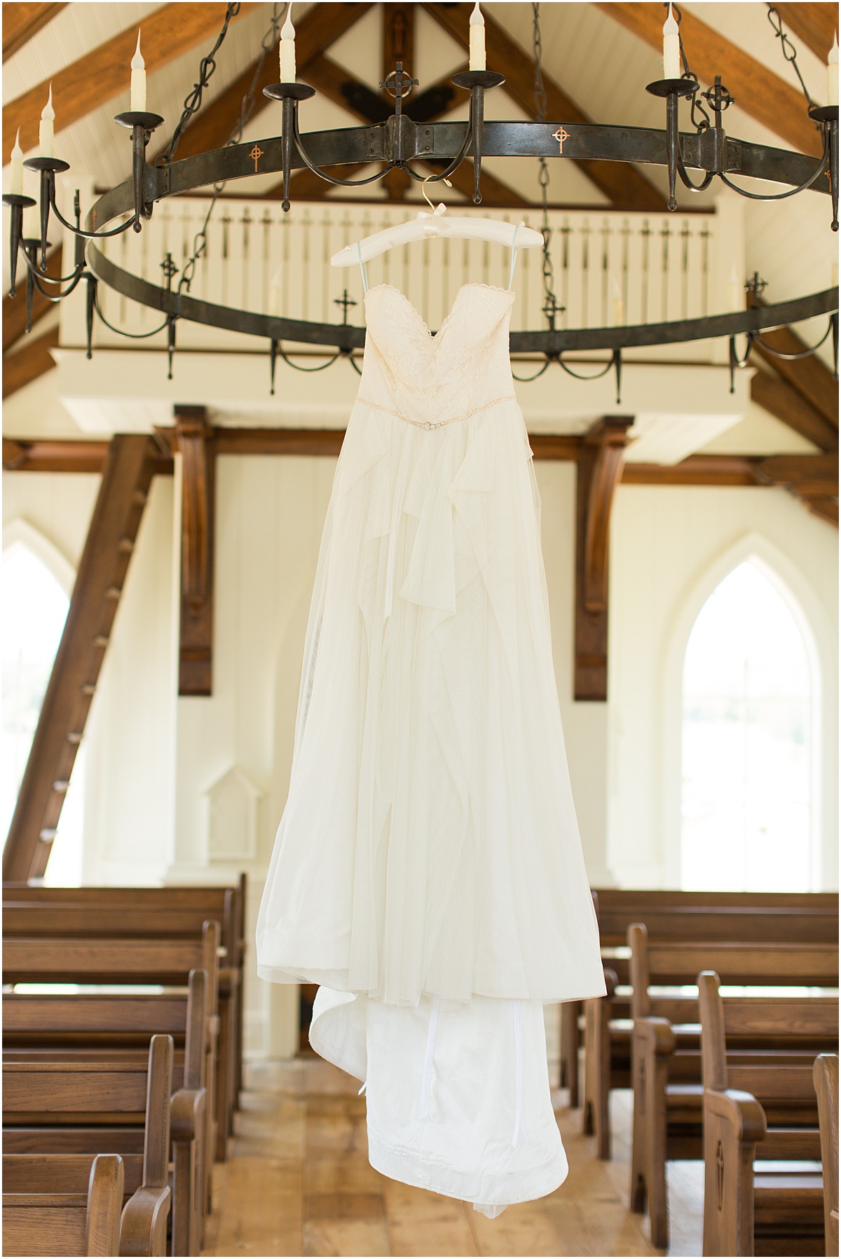 White wedding dress hanging from an iron chandelier in a white chapel