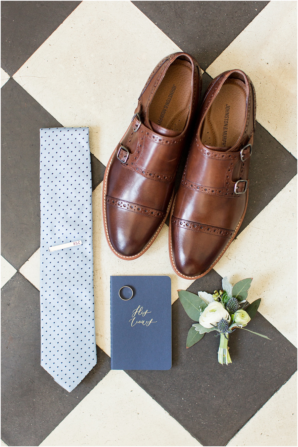 Brown leather shoes with blue tie, silver tie clip and blue vow book in flatlay style