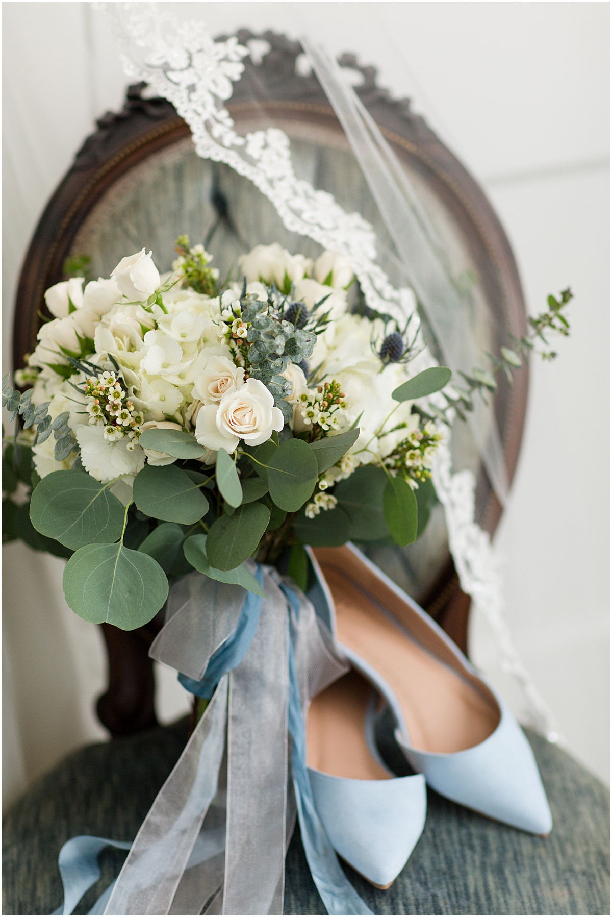 Blue wedding shoes, white bouquet and lace veil sitting on a vintage blue velvet chair